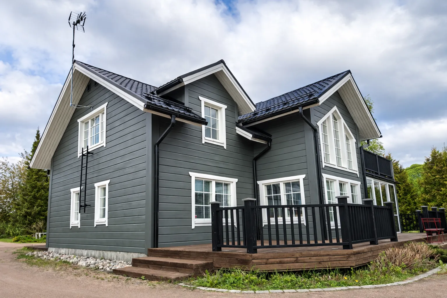 Tummanharmaa puutalo, jossa on valkoiset ikkunat ja musta katto, sekä tikkaat julkisivun huoltoa varten.